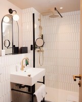A modern bathroom with a white sink, a mirror, a handheld showerhead, and a towel rack.