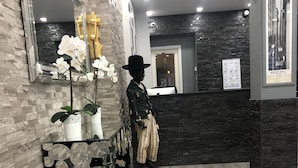 Zona de recepción con pared de piedra, suelo de madera, un maniquí vestido con traje y una orquídea en maceta.