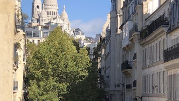 Eine enge Straße mit historischen Gebäuden, ein großer Baum und im Hintergrund ein markantes Gebäude mit Kuppel.