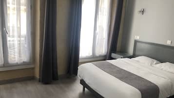 Habitación de hotel con cama, mesita de noche y ventana con cortinas.