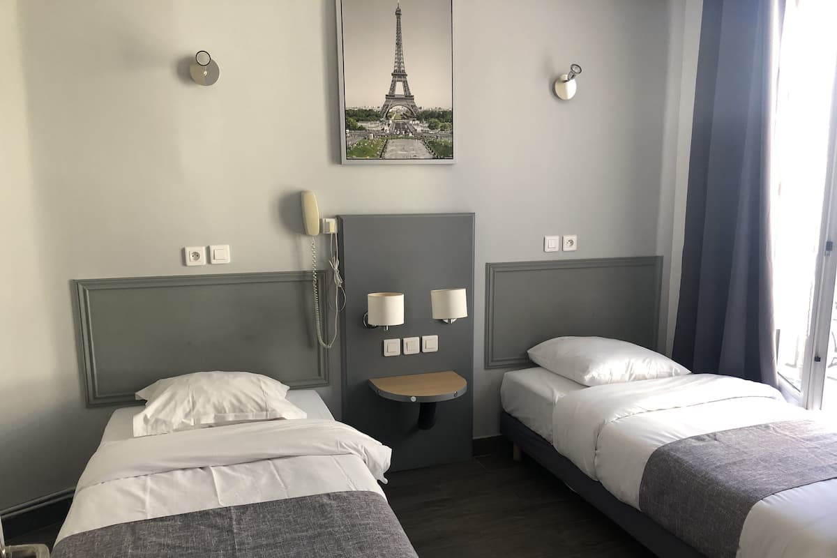 A hotel room with two beds, a small table, a wall-mounted phone, and a picture of the Eiffel Tower.