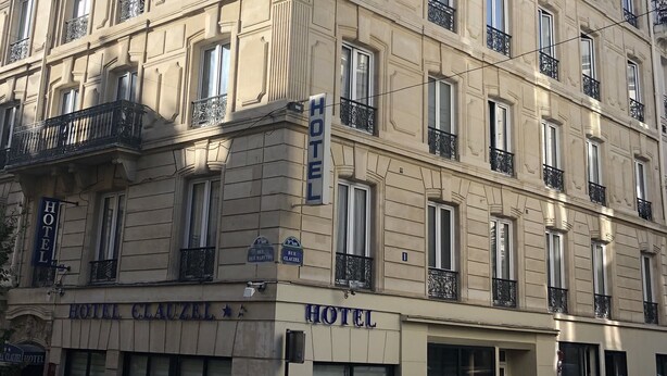 Un hotel de varios pisos con un estilo arquitectónico clásico, que cuenta con balcones con barandillas de hierro forjado y un llamativo letrero que dice "HOTEL CLAUZEI".