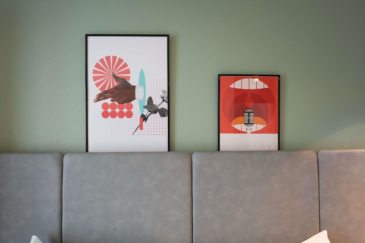 Two framed artworks on a wall above a grey sofa with white cushions.