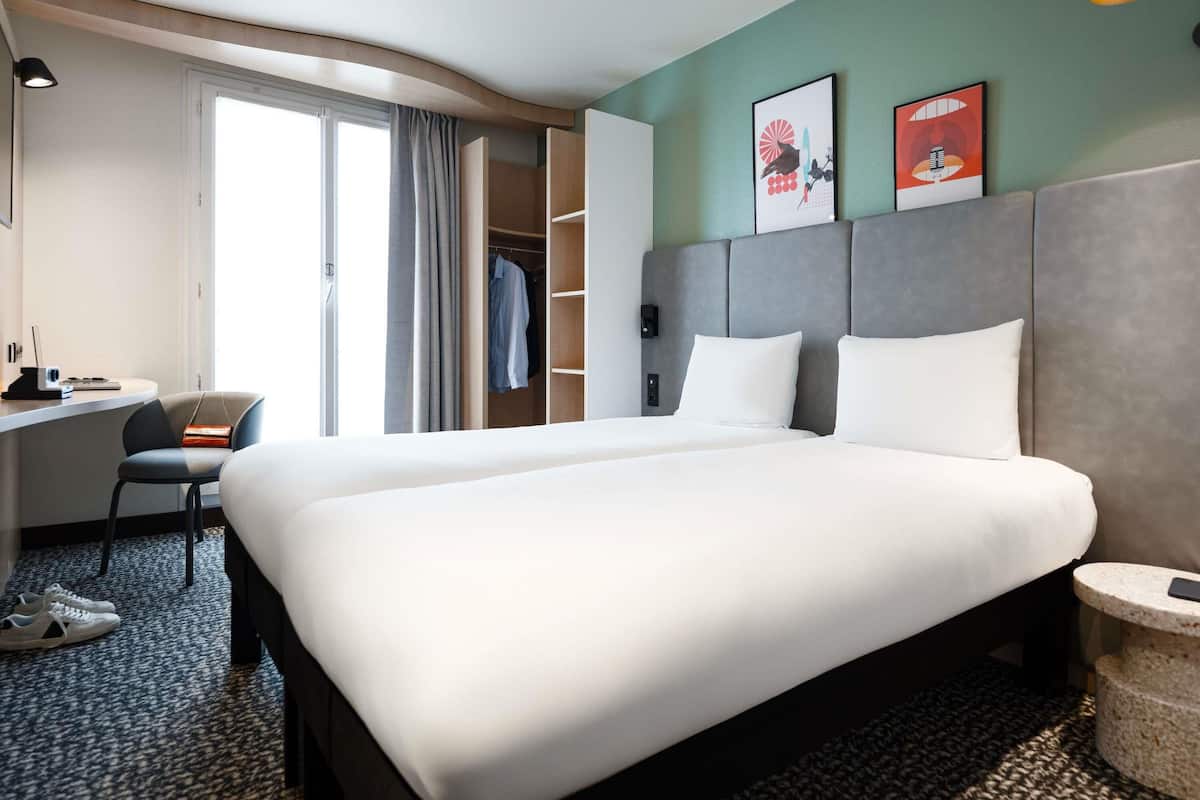 Une chambre d’hôtel avec un grand lit, un bureau avec une chaise, une armoire et une petite table ronde avec un téléphone.