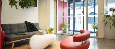 A modern interior with a grey sofa, a white pouf, and a red chair.