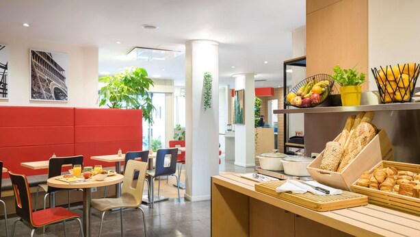 A modern cafe with red booths, round tables, and a variety of food items displayed on the counter.