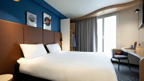 A hotel room with a large bed, a desk, a chair, and a window with curtains.