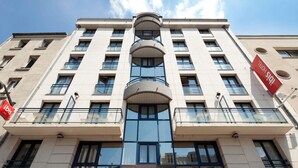 A modern hotel building with multiple balconies, large windows, and a prominent 'ibis' logo.