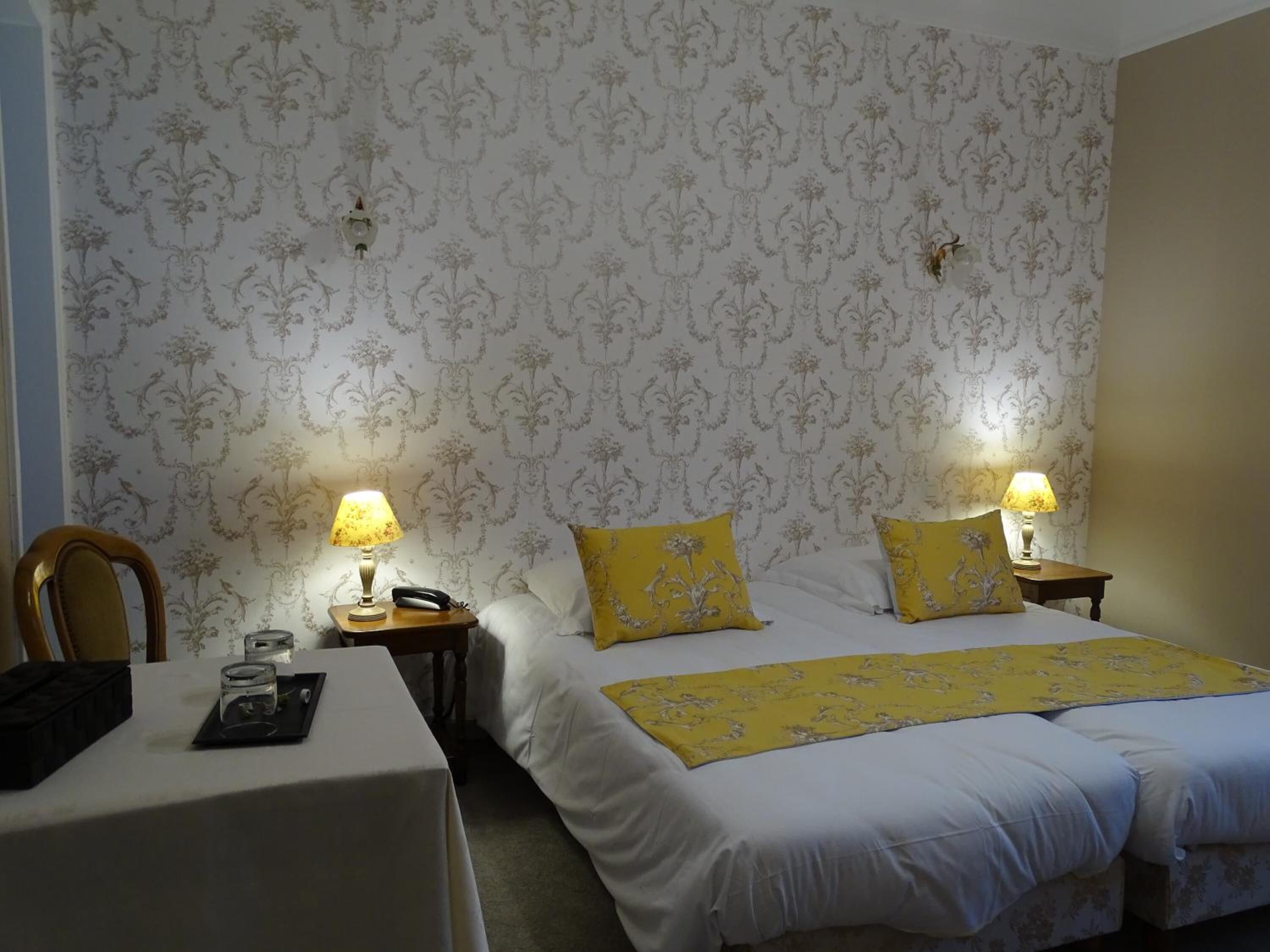 A hotel room with two beds, a table, and two bedside tables with lamps.