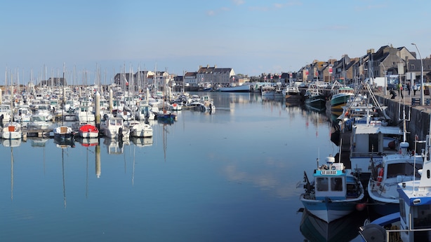 A marina with boats docked along the waterfront, surrounded by buildings and a clear sky.