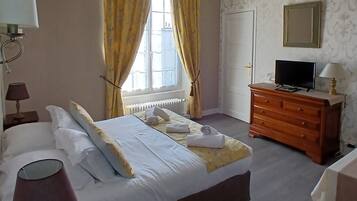 A hotel room with a bed, a dresser, a television, and a window with curtains.