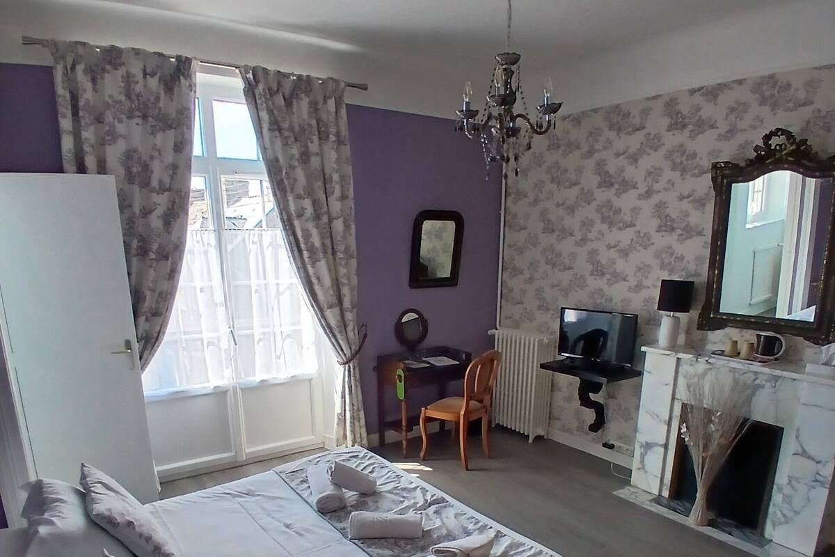 Een slaapkamer met een bed, een bureau, een stoel, een televisie, een spiegel en een open haard.