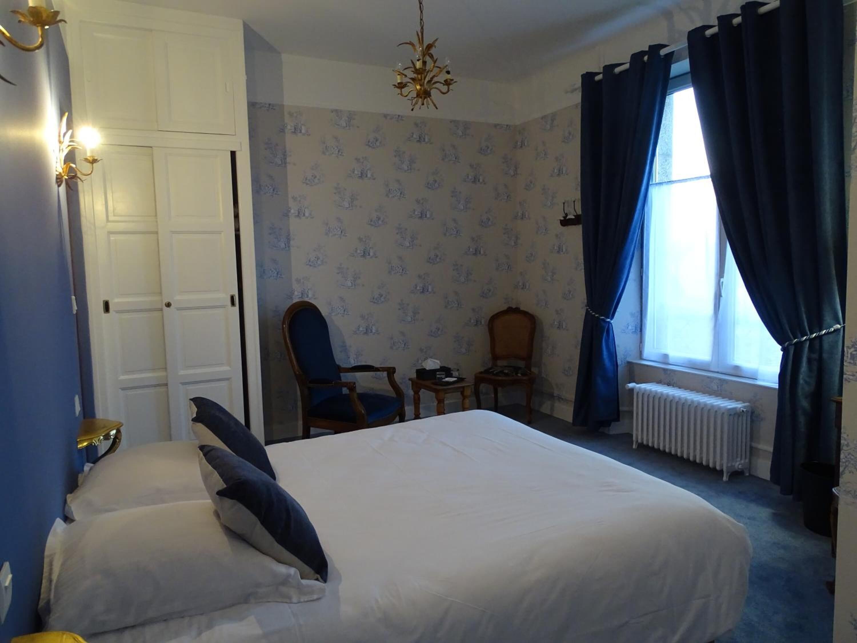 Una camera da letto con un letto grande, una sedia, un tavolino, un termosifone e una finestra con tende.