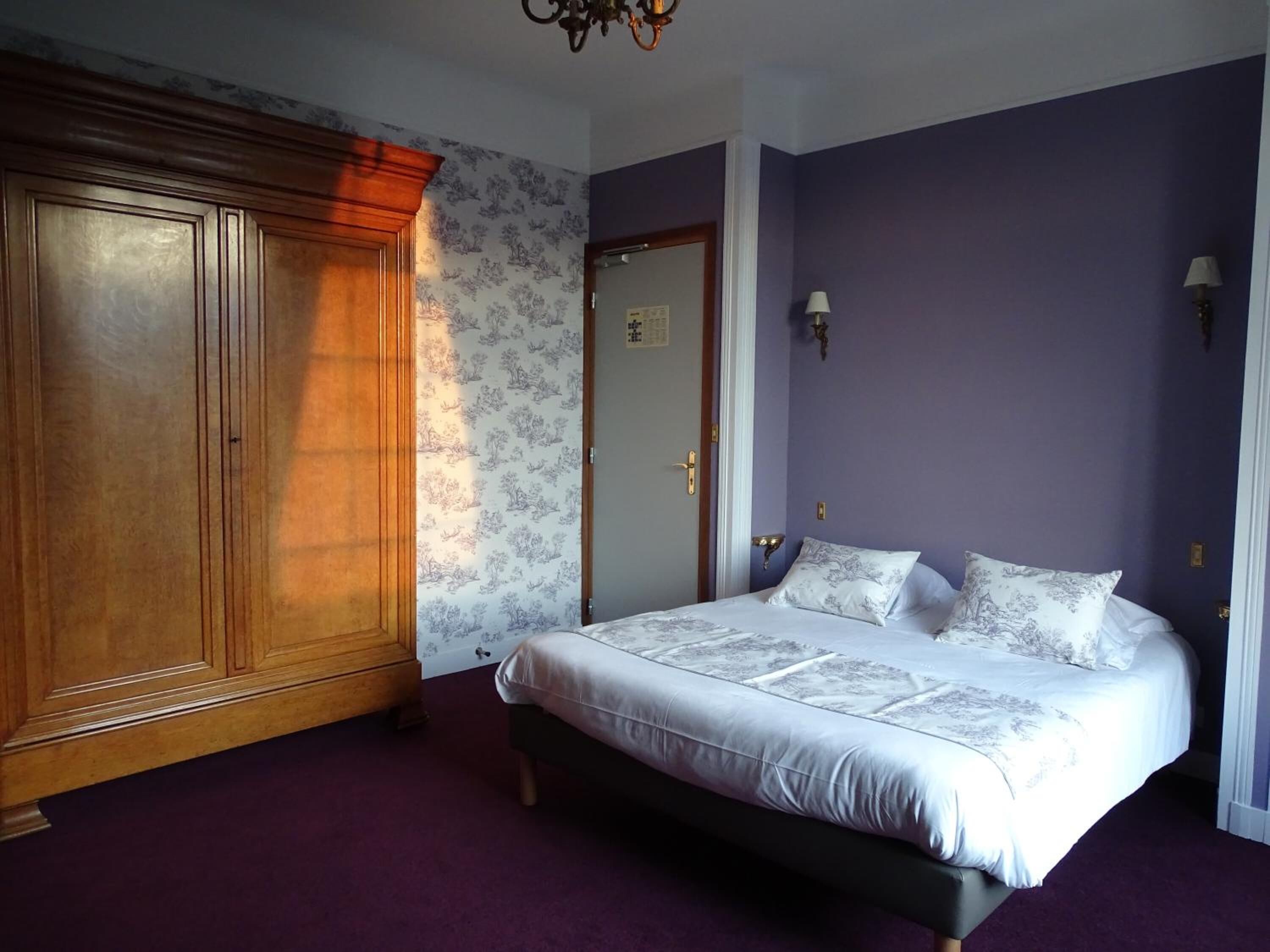 Un dormitorio con un armario de madera grande, una cama con ropa de cama estampada y una alfombra morada.