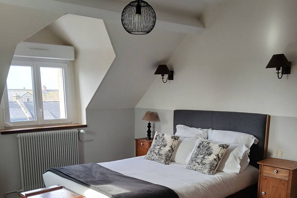 Een slaapkamer met een bed, nachtkastjes, een raam en een hanglamp.