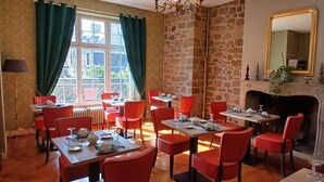 A dining area with multiple tables and red chairs, a stone wall, a chandelier, and a fireplace.