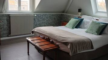 A bedroom with a sloped ceiling, a bed with pillows, a bench, a radiator, and a window.