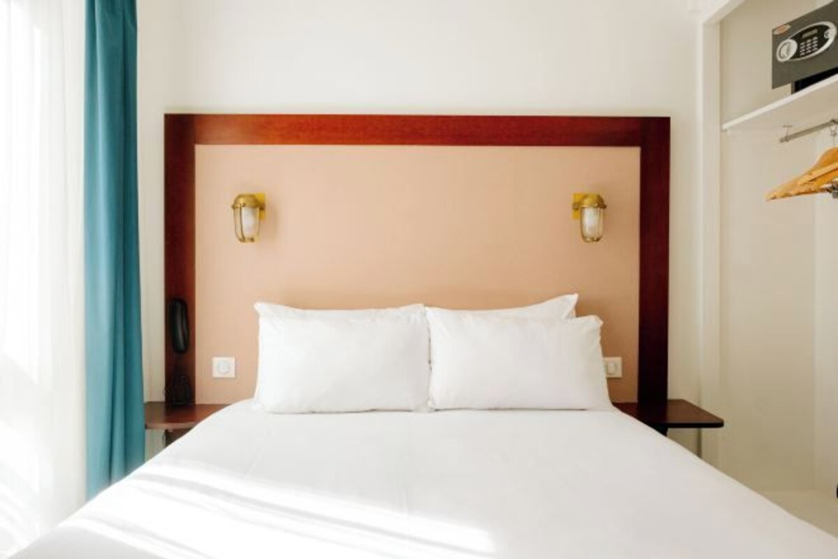 A hotel room with a large bed, two bedside lamps, and a wooden headboard.