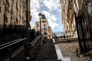 Una escalera conduce a un edificio con una torre del reloj, rodeado de muros de piedra y barandillas de metal.