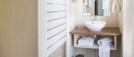 Un baño moderno con un lavabo blanco, encimera de madera y un espejo. Hay dos toallas blancas en el estante y un cubo de basura en el suelo.