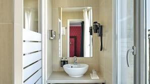 A modern bathroom with a large mirror, a white sink, a towel rack, and a glass shower enclosure.