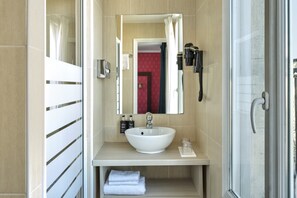 Ein modernes Badezimmer mit großem Spiegel, einem weißen Waschbecken, einem Handtuchhalter und einer Duschkabine aus Glas.