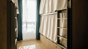 A room with a wooden floor, a window with sheer curtains, and a built-in shelf with a curtain. - Glint Paris (Paris)