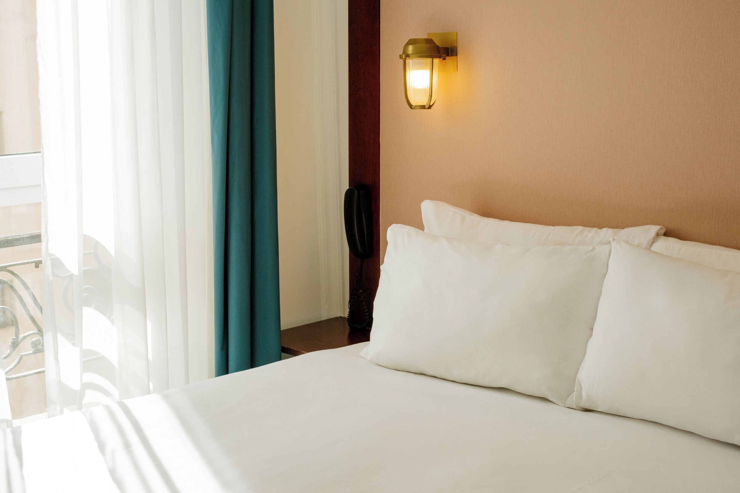 A hotel room with a bed, a wall-mounted light fixture, and a view of the outdoors.