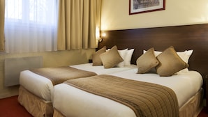 Une chambre d’hôtel avec deux lits, des rideaux beiges, un tableau encadré au mur et un radiateur.