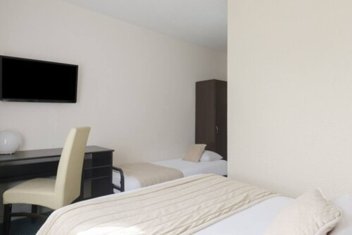 Una habitación de hotel con cama, escritorio, silla, televisor y armario.