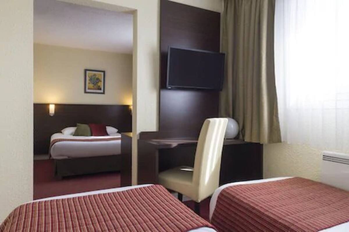 Habitación de hotel con dos camas, un escritorio, una silla, un televisor de pantalla plana y un ventanal con cortinas.