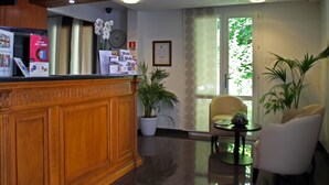 Un espace d’accueil avec un comptoir en bois, des plantes en pot, une horloge et une fenêtre donnant sur un paysage verdoyant.