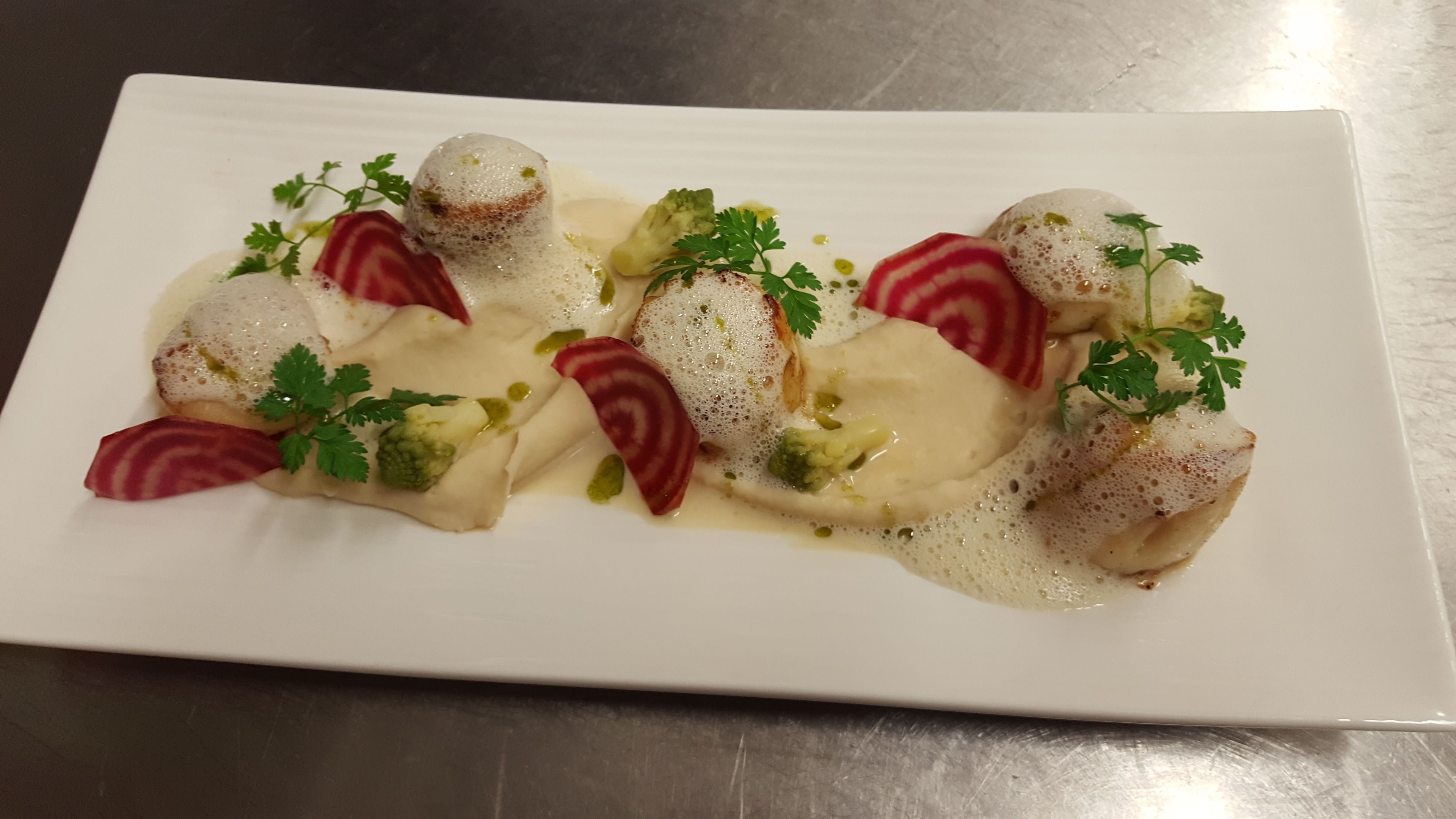 A white rectangular plate with a dish of food, garnished with parsley and beet slices, on a metallic surface.