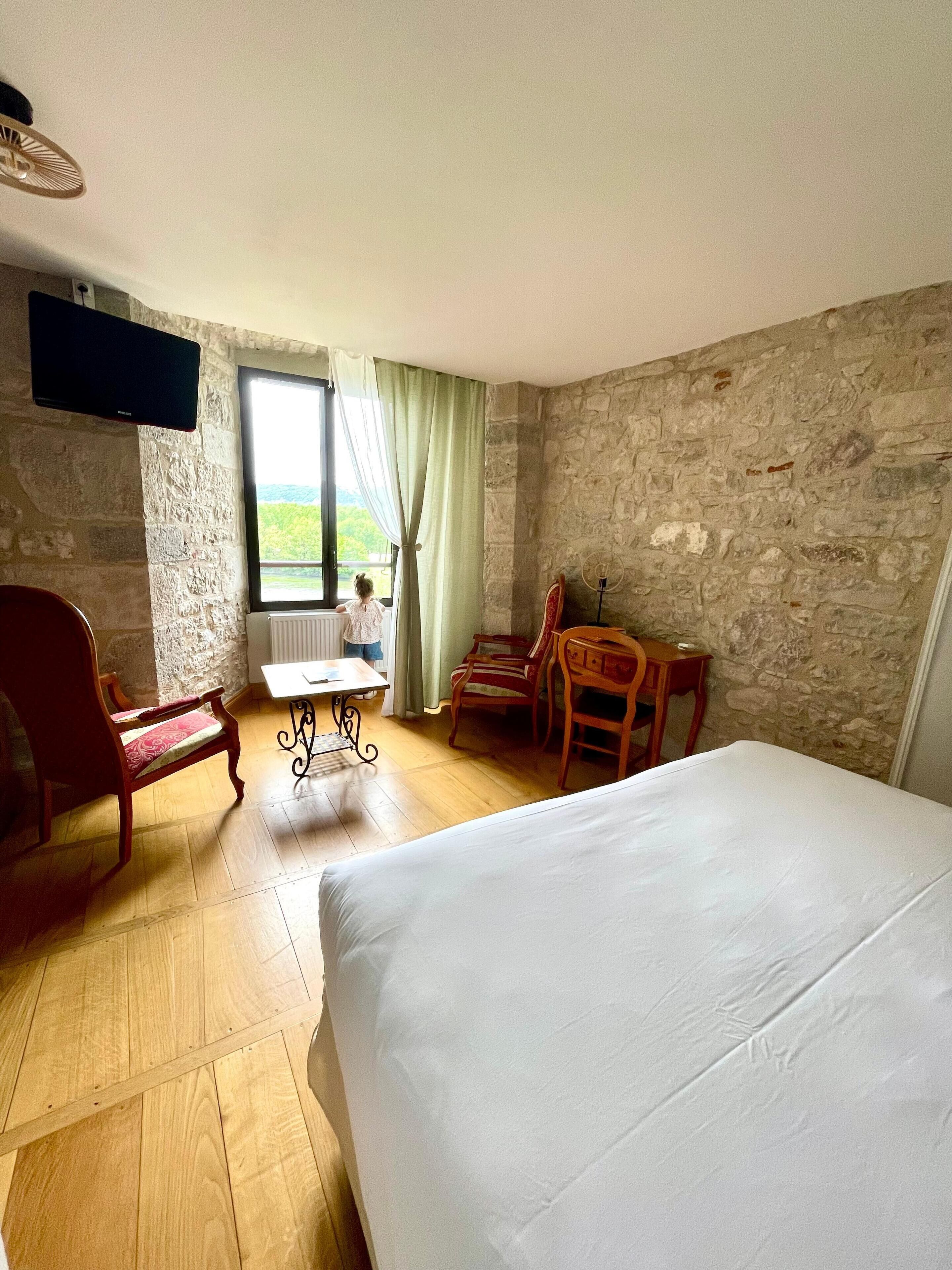 Ein Zimmer mit einem Bett, einem Tisch, Stühlen, einem Fernseher und einem Fenster mit Vorhängen.