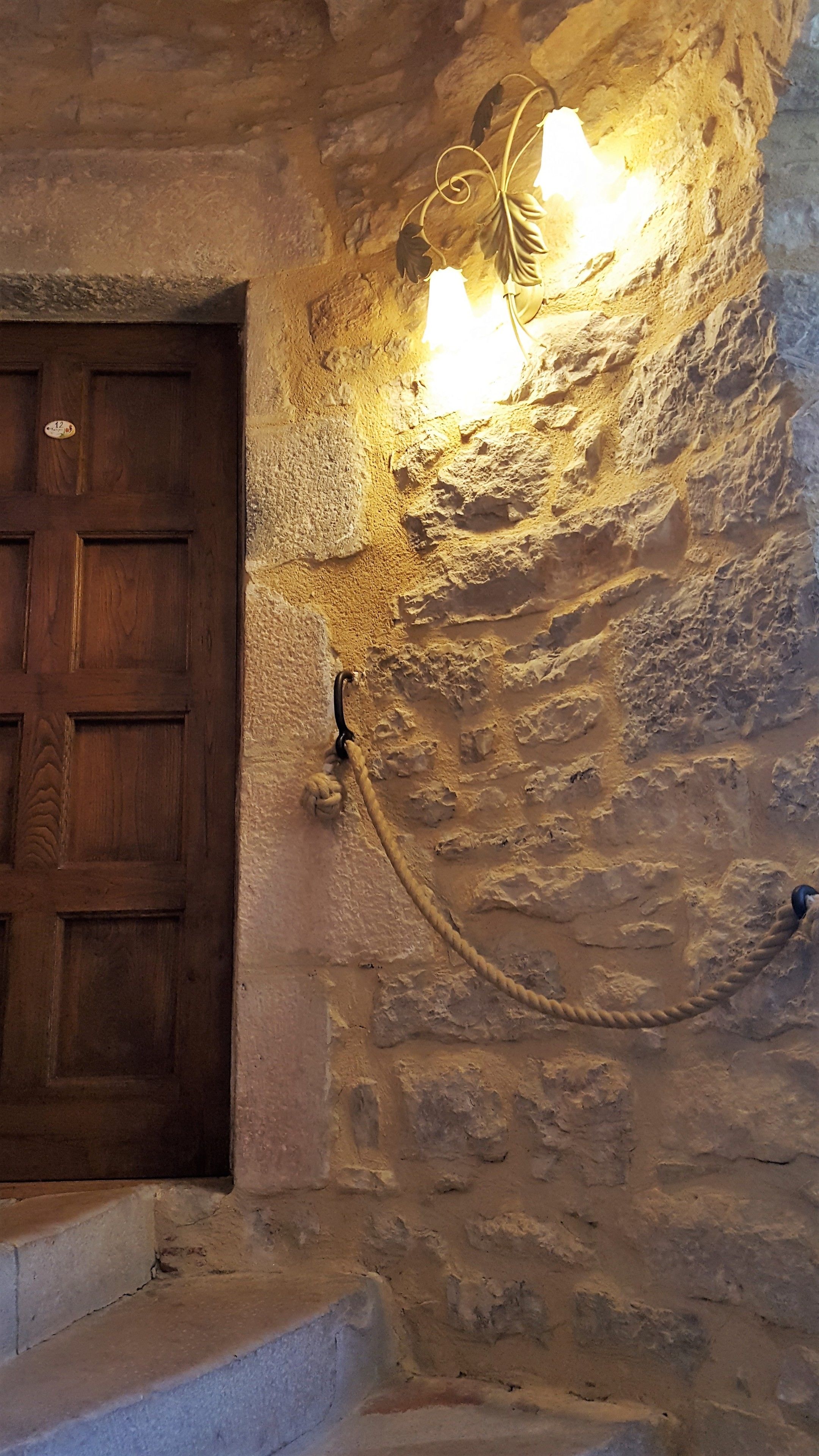 A rustic stone wall with a wooden door and a wall-mounted light fixture.
