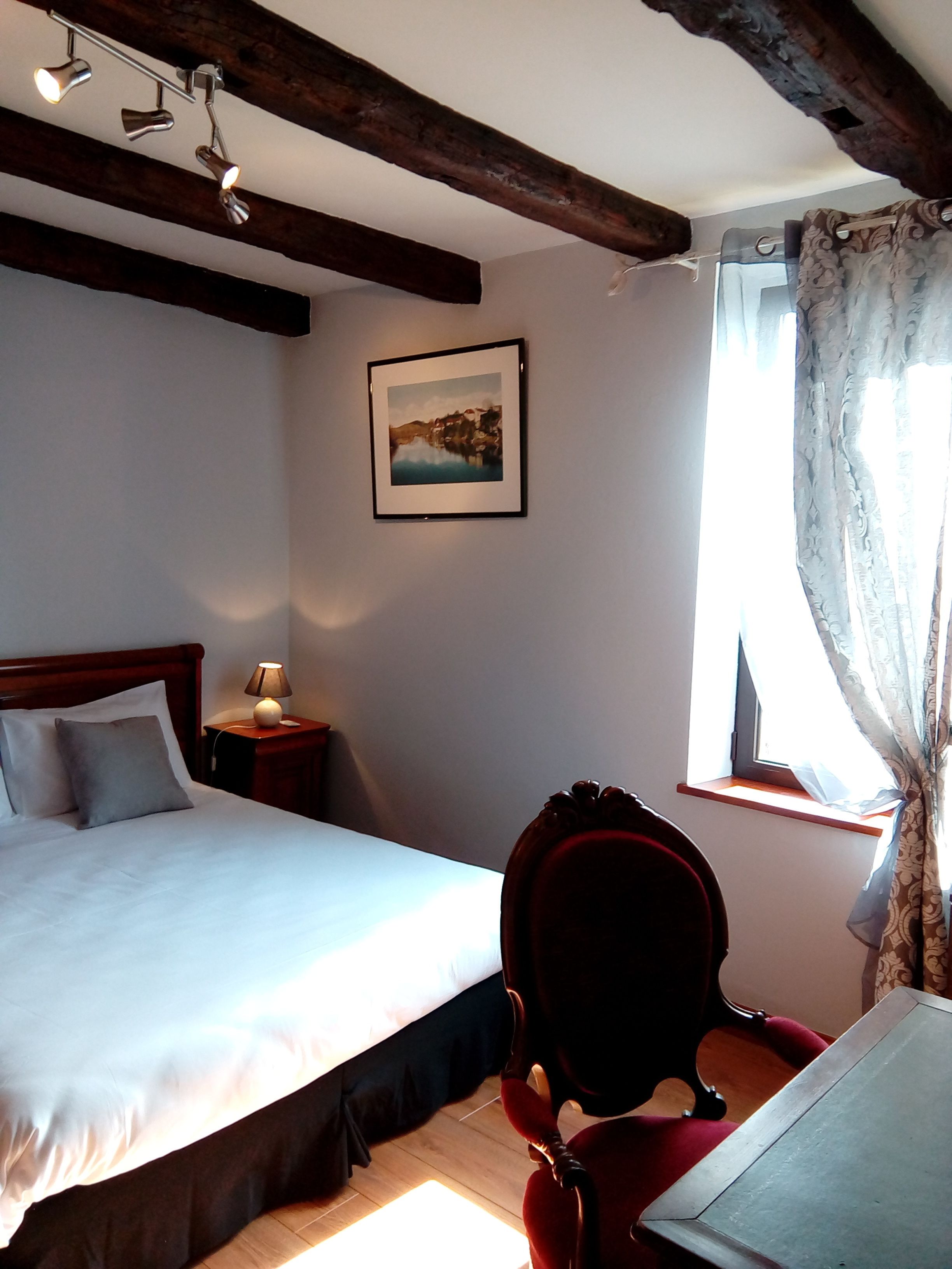 A bedroom with a bed, a nightstand, a chair, a window with curtains, and a framed picture on the wall.