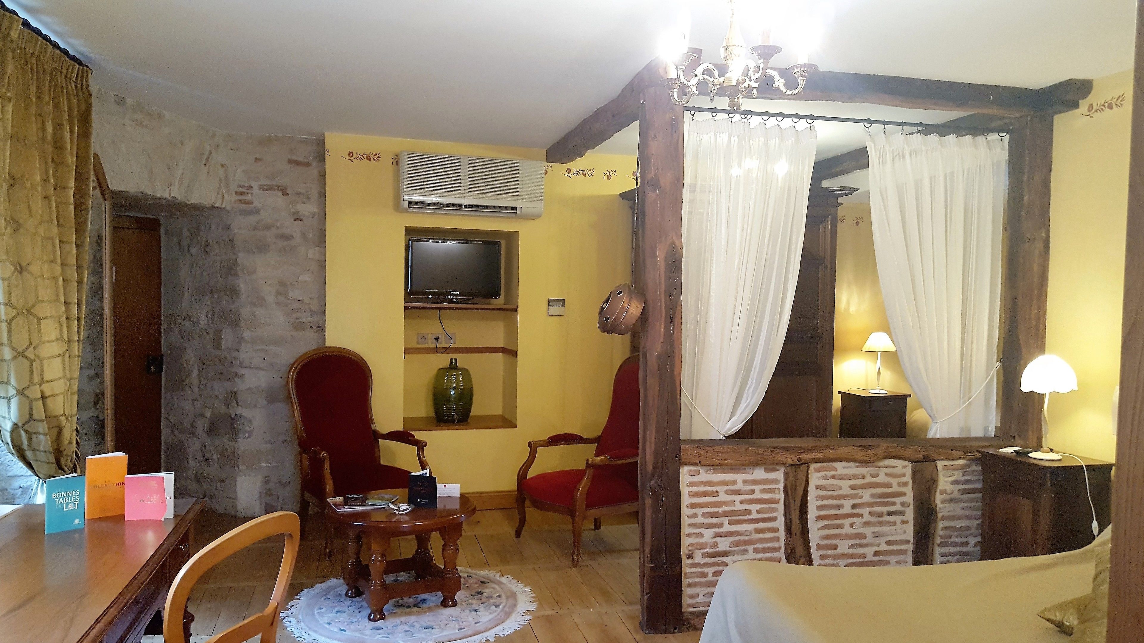 A cozy room with a brick wall, a wooden chair, a table with a lamp, and a TV mounted on the wall.