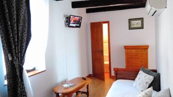 A bedroom with a wooden bed, a wooden nightstand, a wooden bench, a television on the wall, and a door leading to another room.