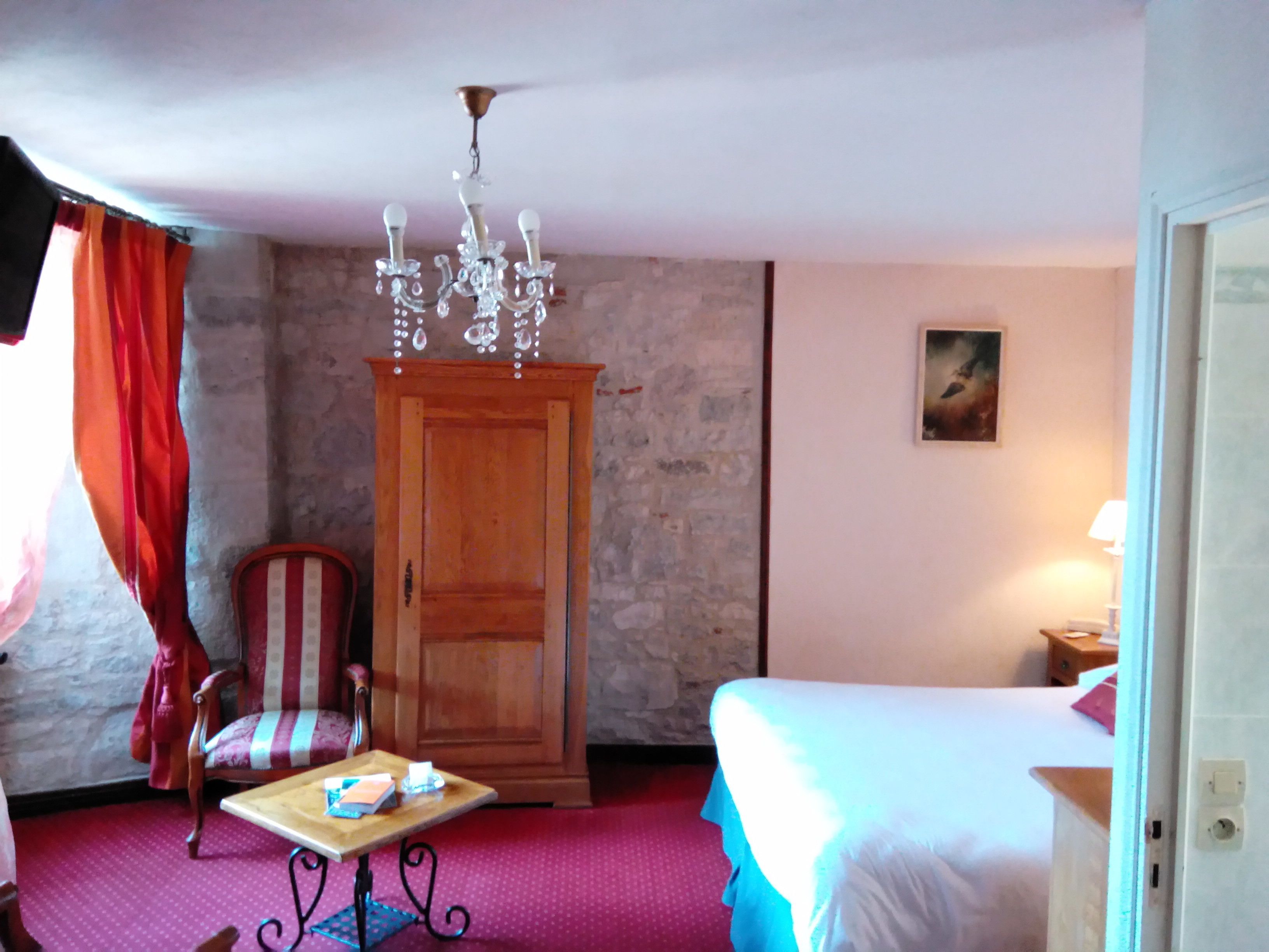 Una habitación de hotel con cama, un armario de madera, una silla, una mesita pequeña y una araña.
