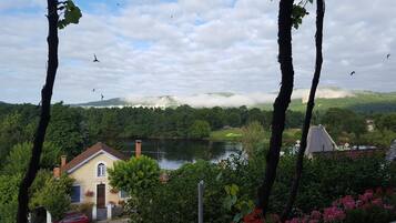 A house with a garden and a lake, surrounded by trees and mountains.