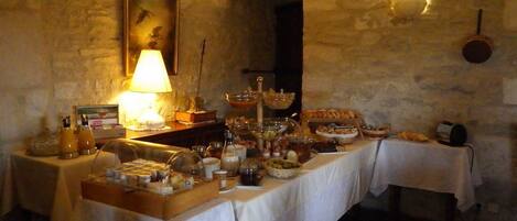 A dining area with stone walls, a table set with various dishes, a lamp, and a framed picture on the wall.
