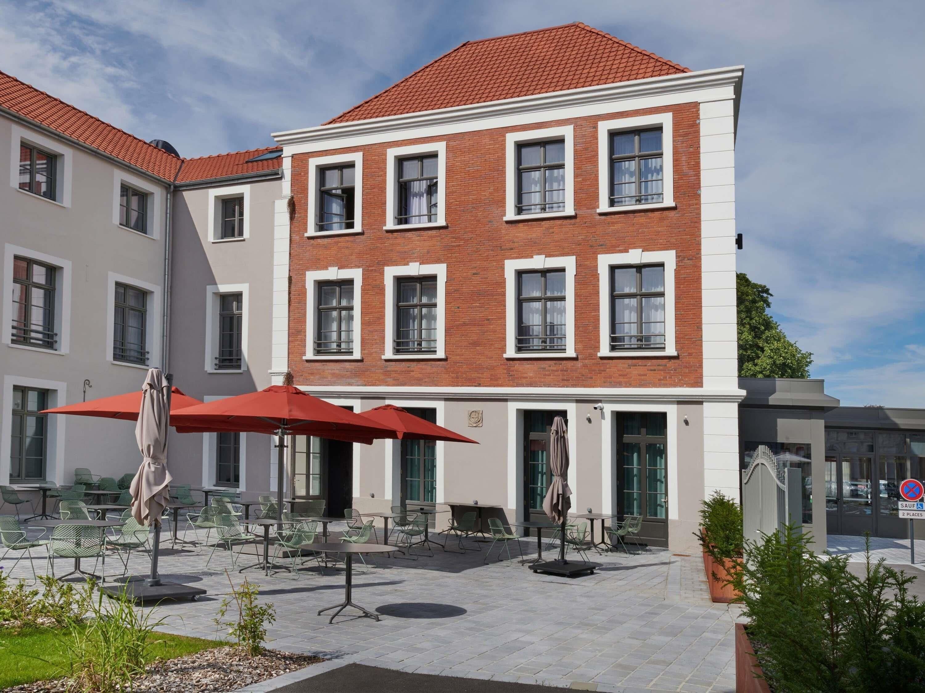 A multi-story building with a red-tiled roof, a courtyard with outdoor seating, and a sign indicating parking restrictions.