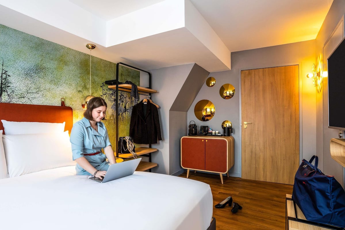 A modern hotel room with a bed, a desk, a wardrobe, and a mirror with circular reflections.