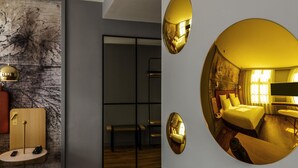 Habitación de hotel moderna con un espejo grande que refleja el interior de la habitación, una mesita de madera con un teléfono y un ventanal con cortinas.