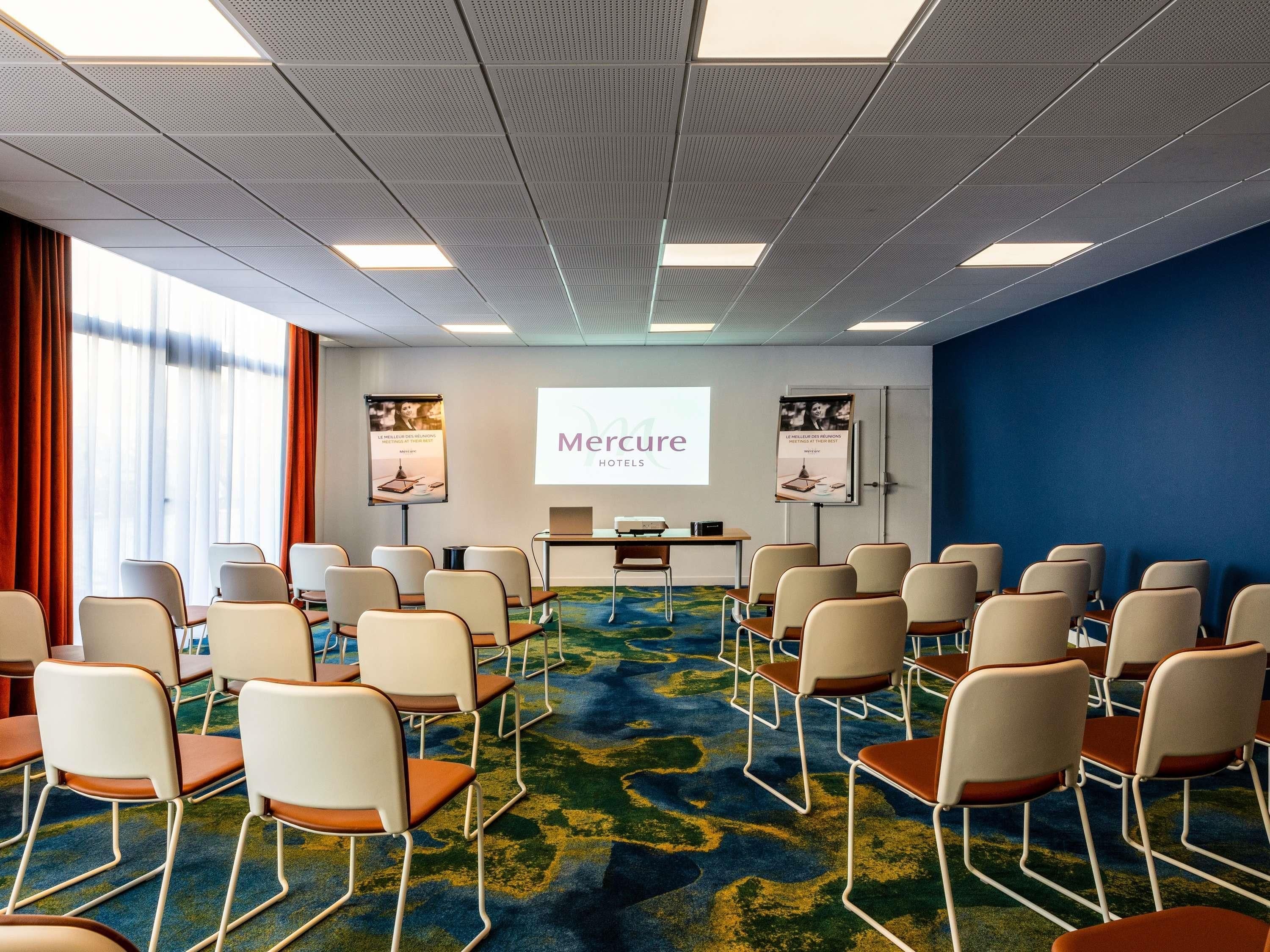 A conference room with rows of chairs, a projector screen, and two posters on the walls.