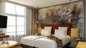 Habitación de hotel con cama doble, escritorio con computadora portátil, televisión y un amplio ventanal con cortinas.