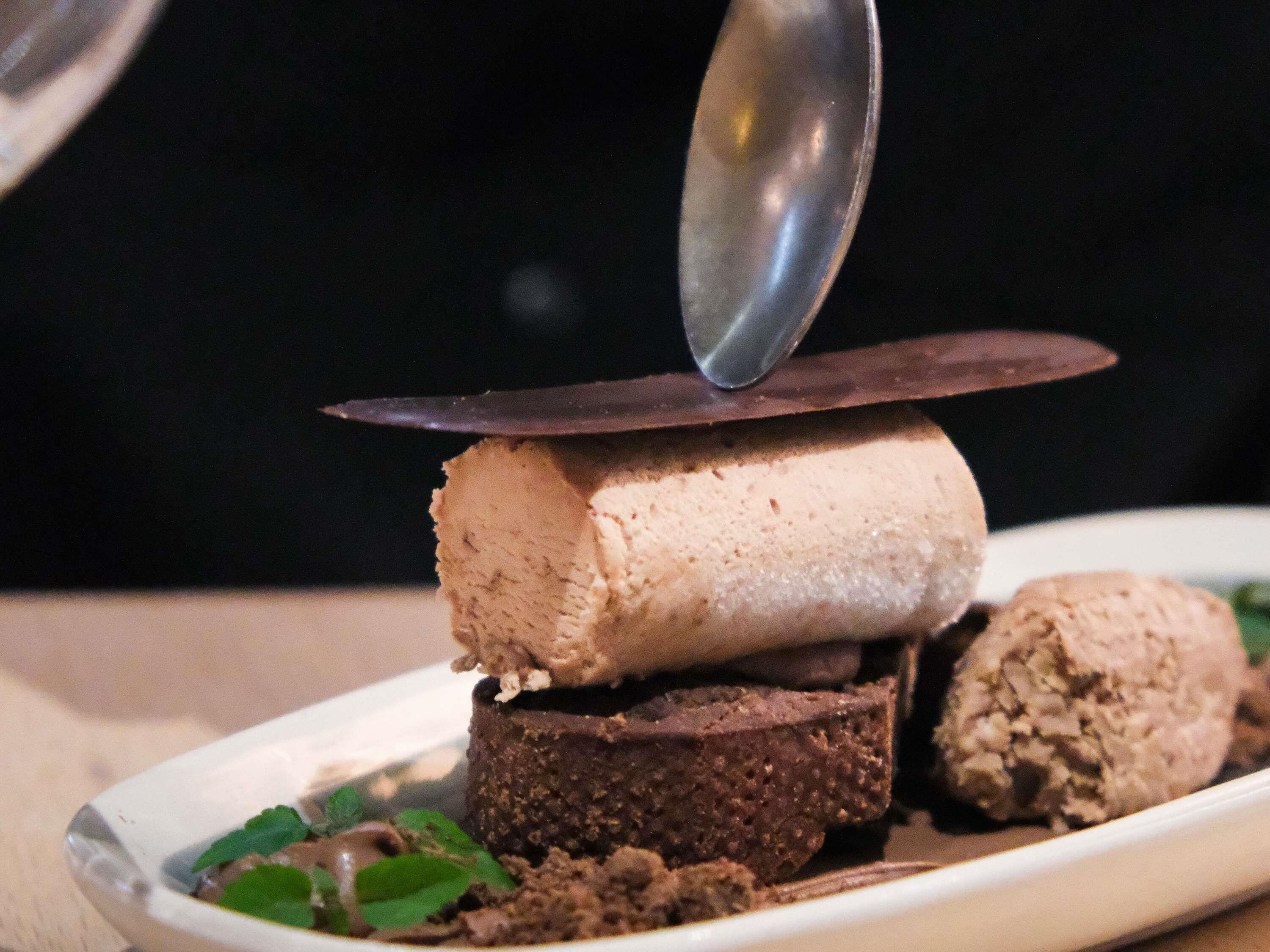Een dessert met meerdere lagen ijs en chocolade, geserveerd op een wit bord met een lepel erbovenop.
