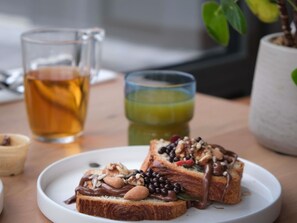 A plate with toast topped with various nuts and chocolate, a glass of tea, and a glass of green juice on a wooden table. - Mercure Saint Omer Centre Gare  (Saint-Omer)