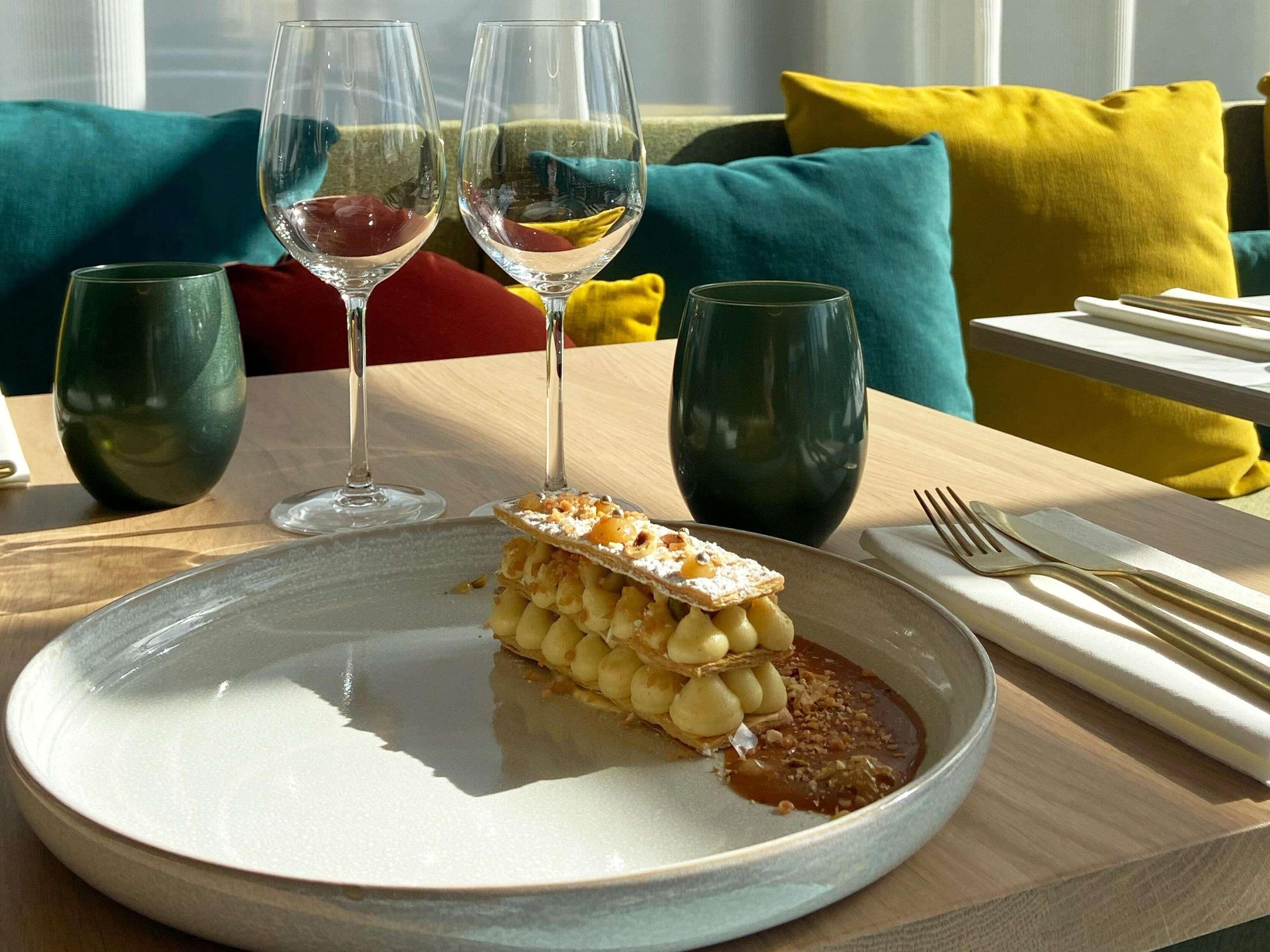 Una mesa de comedor con un plato de postre, dos copas de vino y cubiertos.