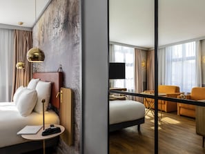 Habitación de hotel con cama, mesita de noche, lámpara y un espejo grande que refleja la habitación.